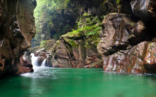 Image water falls between brown rocky mountain during daytime