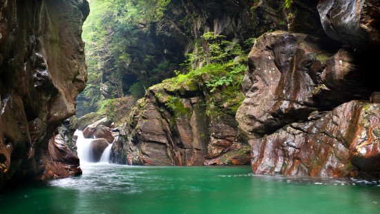 Image water falls between brown rocky mountain during daytime