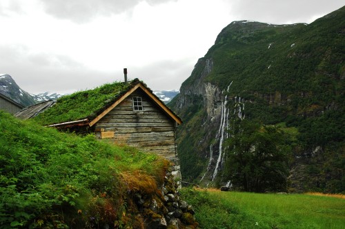 Image brown wooden house on green grass field near mountain during daytime