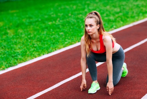 Image woman in black tank top and green shorts running on track field during daytime