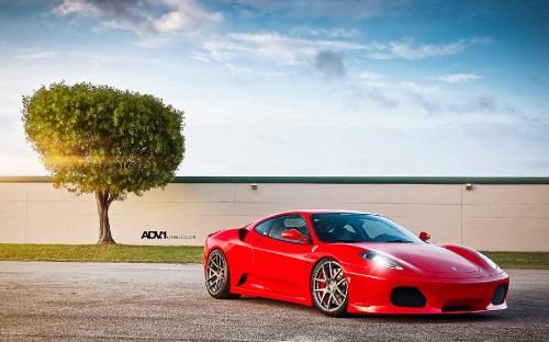 Image red coupe parked near green tree under white clouds and blue sky during daytime