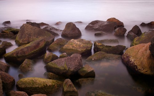 Image gray and green rocks on body of water during daytime