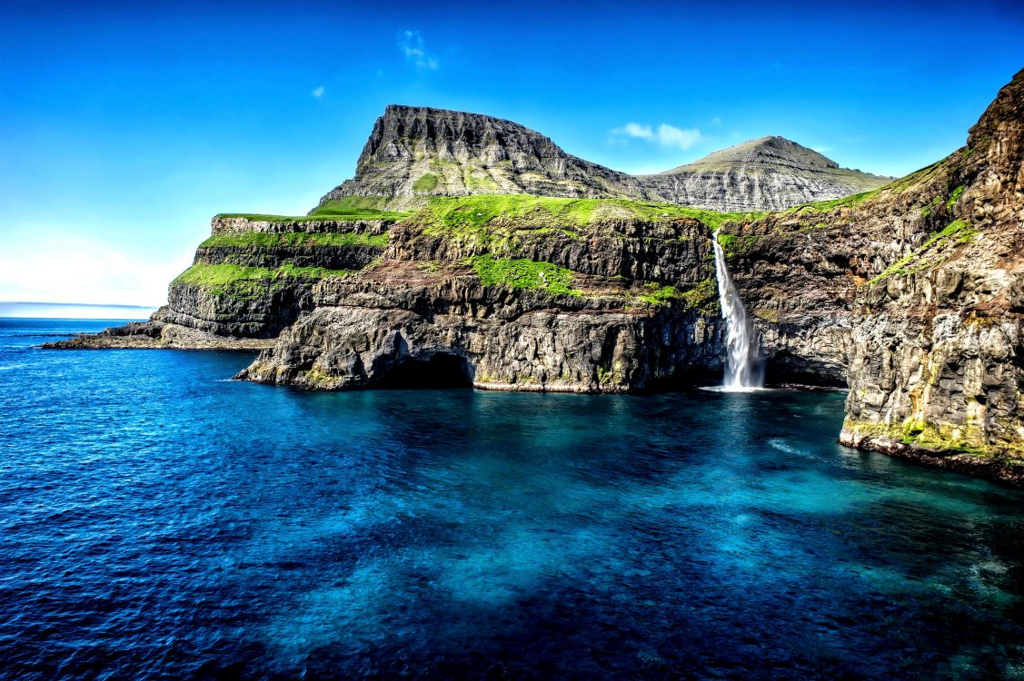 green and brown mountain beside blue sea under blue sky during daytime