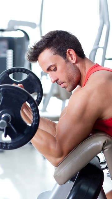 Image man in red tank top sitting on black and gray exercise equipment
