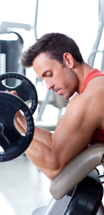 Image man in red tank top sitting on black and gray exercise equipment
