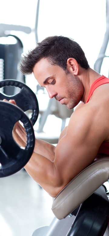 Image man in red tank top sitting on black and gray exercise equipment