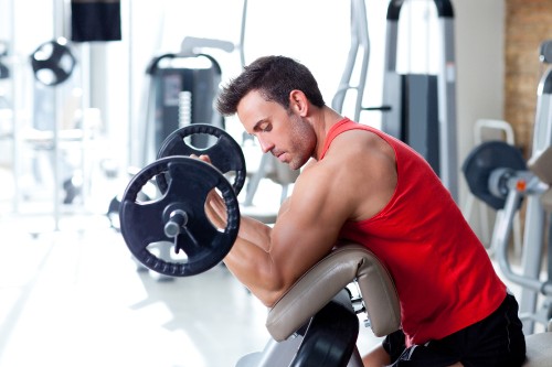 Image man in red tank top sitting on black and gray exercise equipment