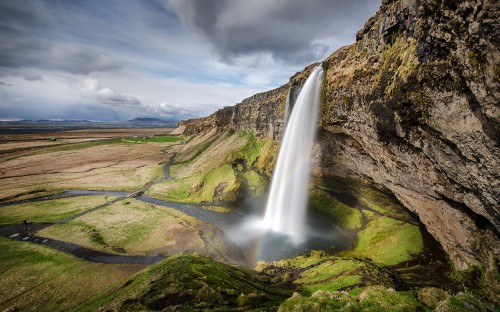 Image waterfalls on green grass field under gray cloudy sky during daytime