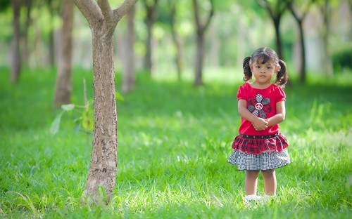 Image girl in red dress standing beside tree