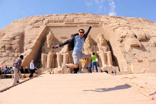 Image man in black jacket and blue denim jeans standing on brown sand during daytime