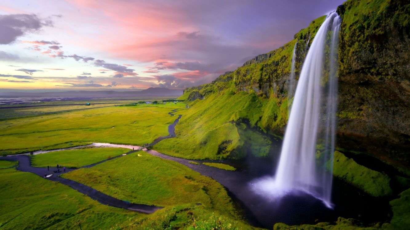 green grass field near waterfalls during daytime