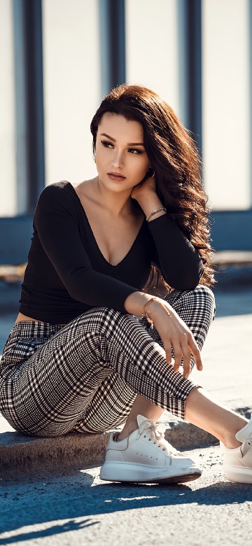 Image woman in black long sleeve shirt and black and white striped skirt sitting on concrete floor