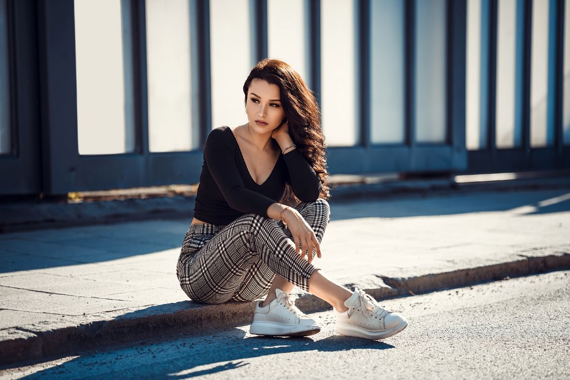 woman in black long sleeve shirt and black and white striped skirt sitting on concrete floor