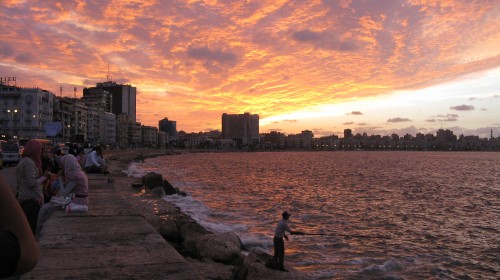 Image man sitting on rock near body of water during sunset