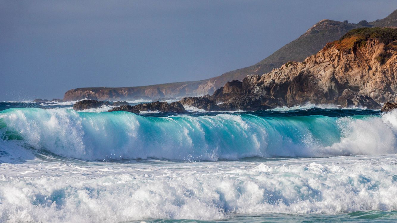 Les Vagues de L'océan S'écrasent Sur Une Formation Rocheuse Brune Sous un Ciel Gris. Wallpaper in 2560x1440 Resolution