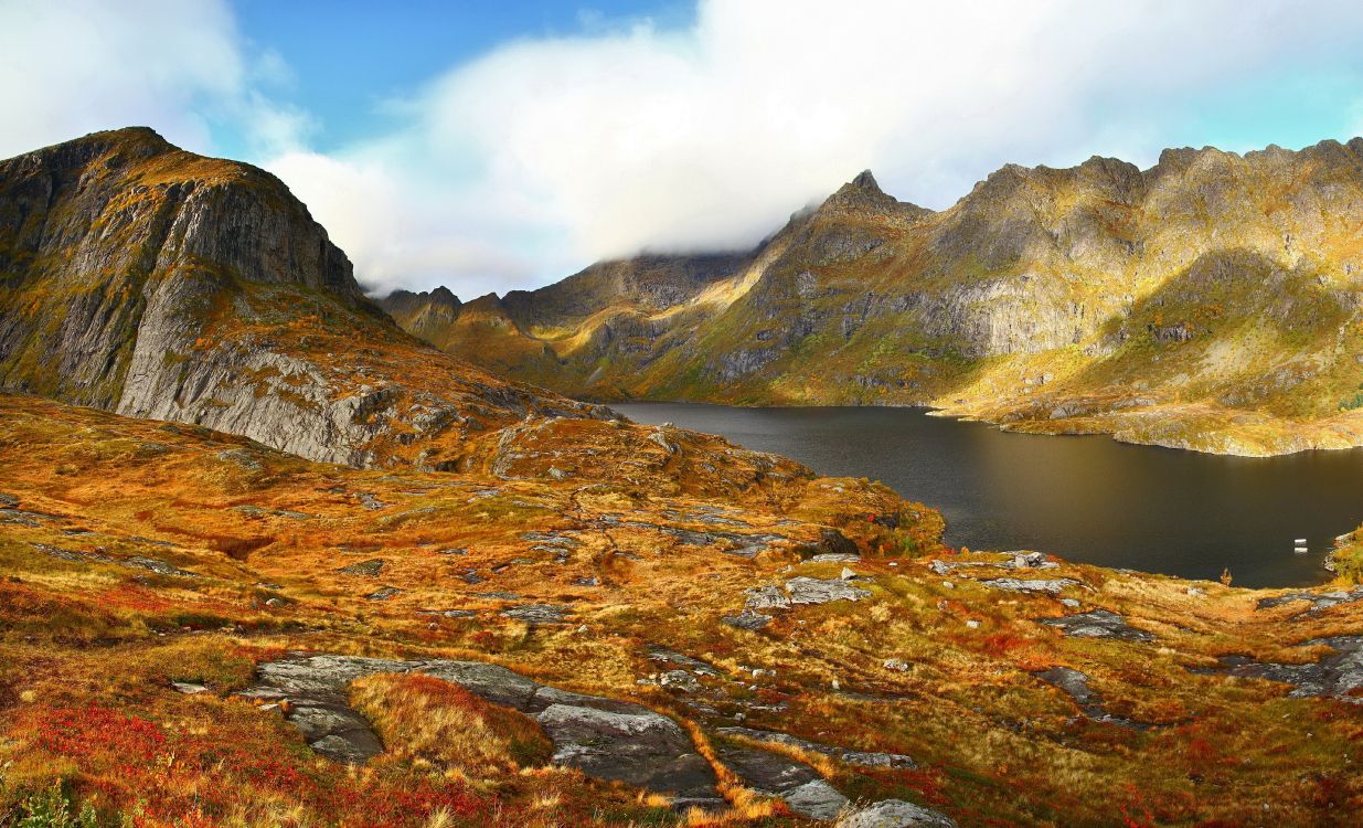 brown and green mountain beside lake under blue sky during daytime