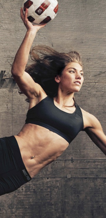 Image woman in black sports bra and black shorts holding white and red soccer ball