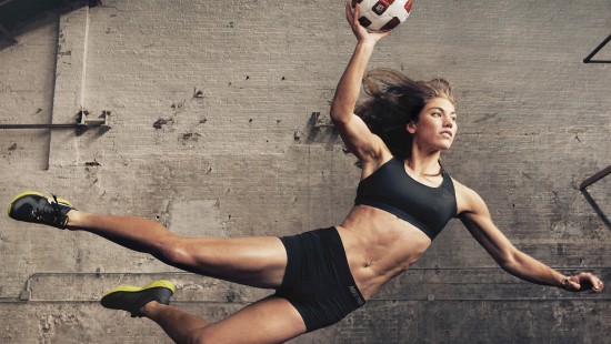 Image woman in black sports bra and black shorts holding white and red soccer ball