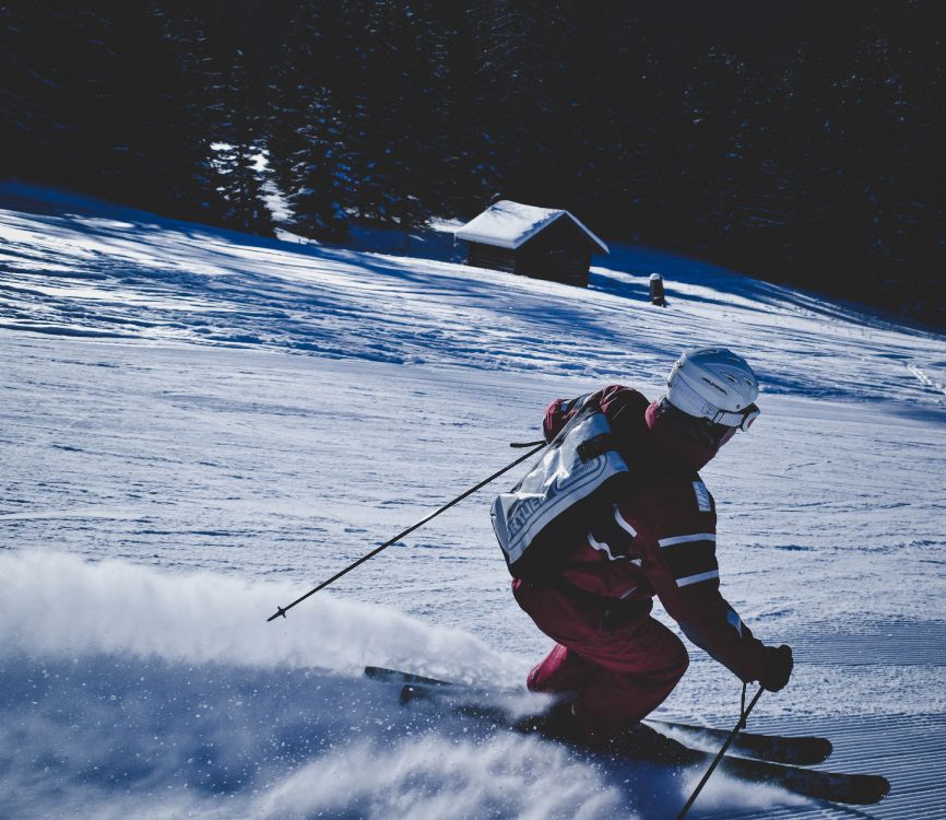 man in red and black jacket and black pants riding ski blades on snow covered ground