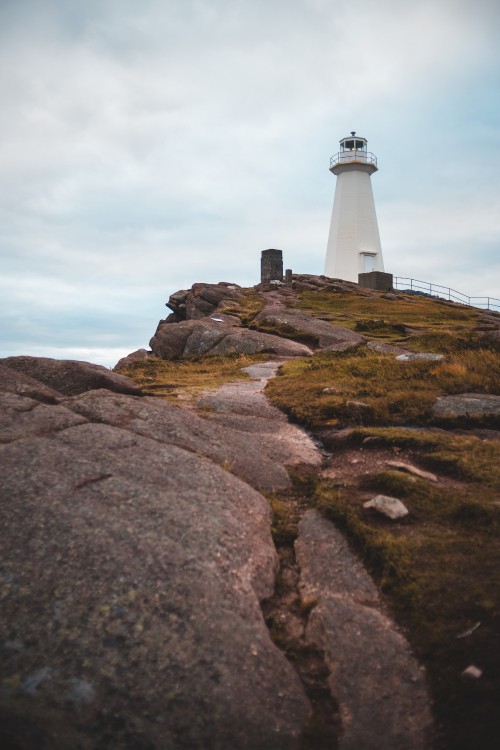 Image white and black lighthouse on brown rocky hill under white cloudy sky during daytime