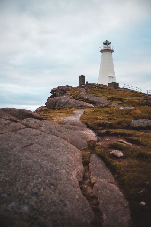 white and black lighthouse on brown rocky hill under white cloudy sky during daytime