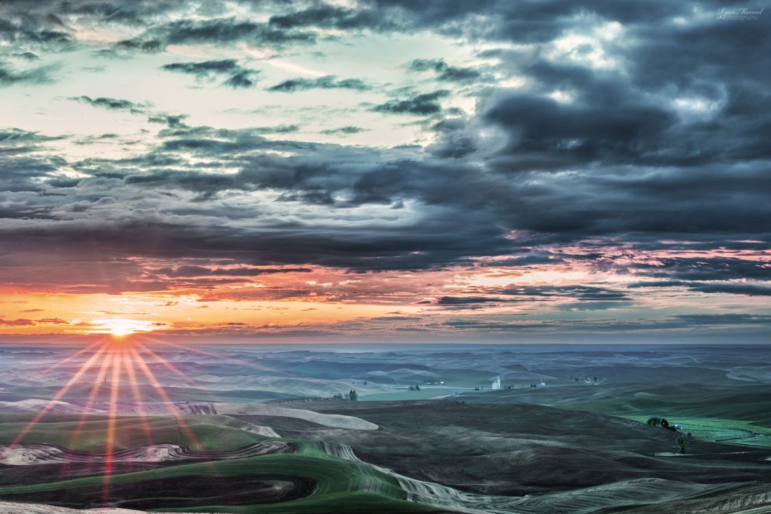 green grass field near sea under cloudy sky during sunset